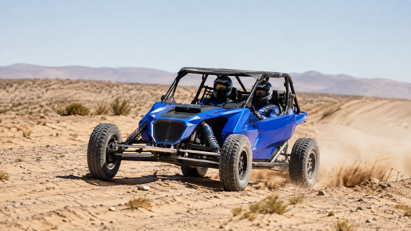 Blue two-seat off-road buggy with an exposed roll cage and suspension moving across uneven sand