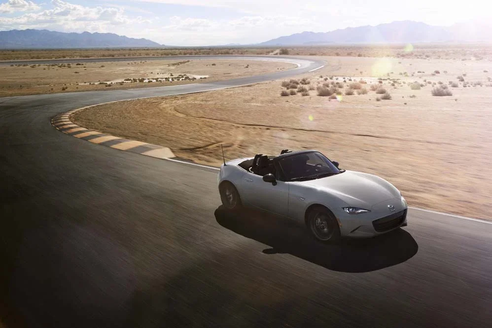 Grey Mazda MX-5 Miata soft top driving on a desert road