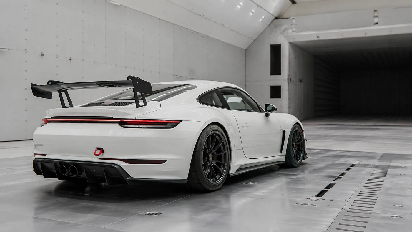 White sports coupe with a raised rear wing and low rear diffuser in a bright aerodynamic test hall