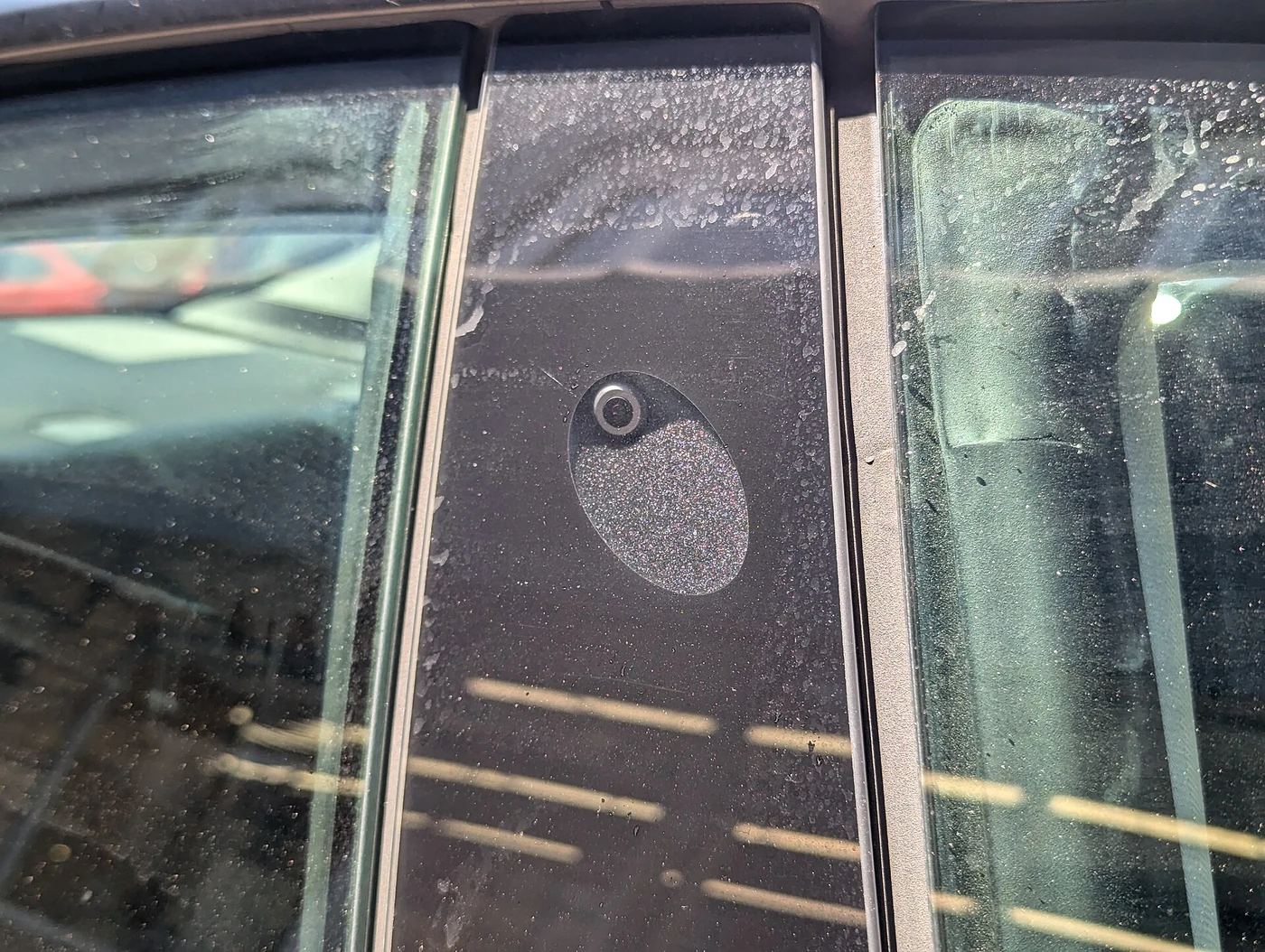 Tesla passenger-side B-pillar camera with its circular lens visible behind the exterior cover