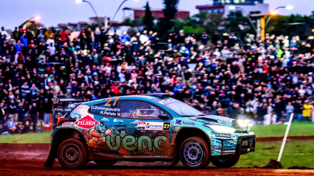 WRC rally car passing a large crowd beside a special stage